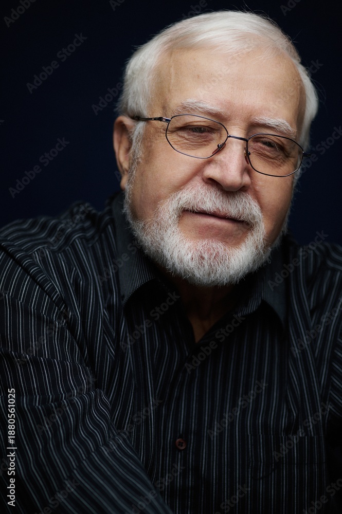 Obraz premium Elderly man with glasses poses for a portrait with a gentle smile in a studio setting