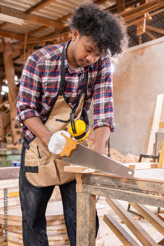 Carpenter cutting wood with handsaw in workshop