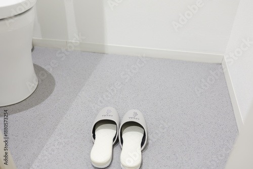 Foto 清潔なトイレ空間に並ぶスリッパと便器の一部。
