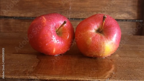 Two juicy red apples on a rustic wooden table, being moistened with water.