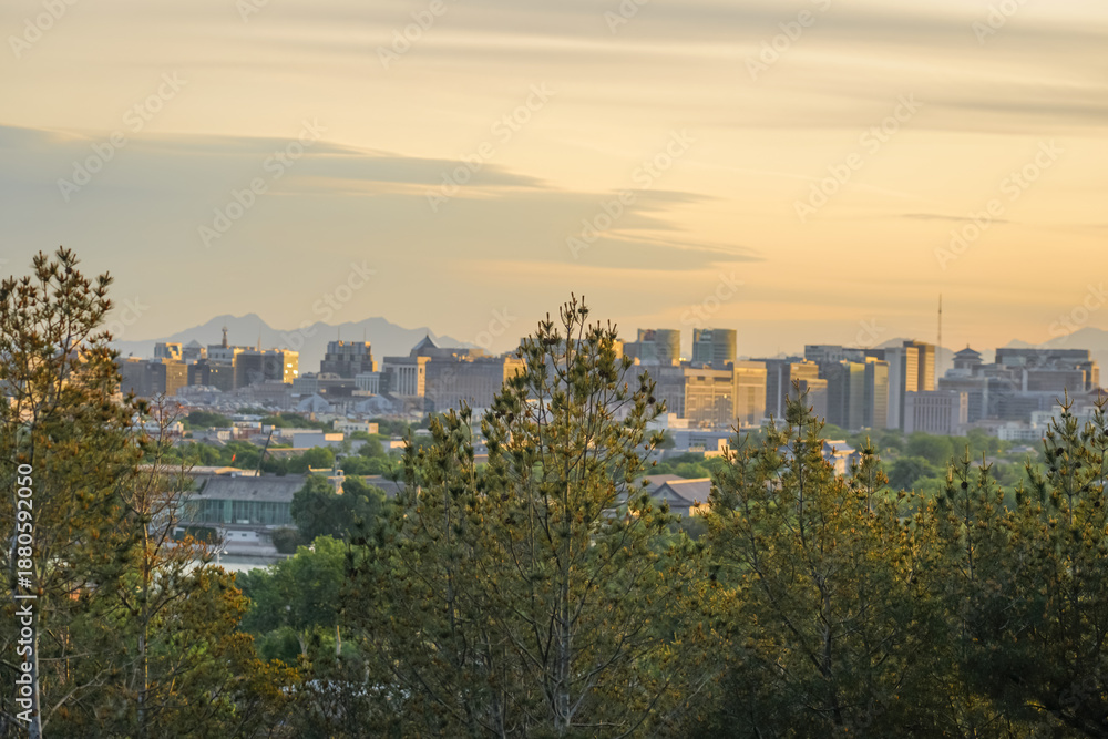 Obraz premium City skyline at sunset viewed from a forested hilltop with distant mountains in the background
