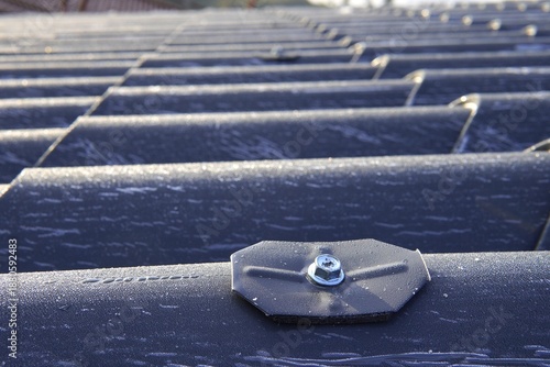 Roofing sandwich panels. Installation of insulated metal sandwich panels. Top view of anthracite-gray metal roofing panels with a tile texture. Bolts with EPDM washers.
