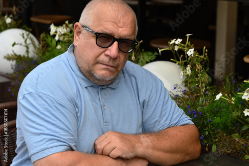 Принти на полотні Portrait of Caucasian elderly gray-haired man wearing glasses and blue T-shirt at table in street cafe