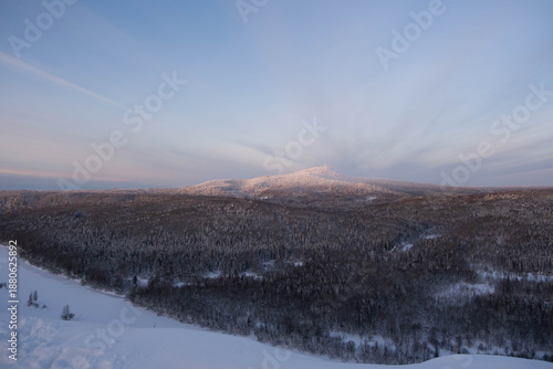 Snow-covered cap of the Polyud Mountain, shining brightly in the rays of the dawn sun. Perm Region