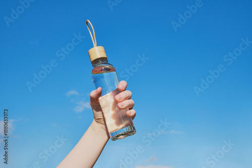Hand holding reusable glass water bottle with water for hydration and sustainability