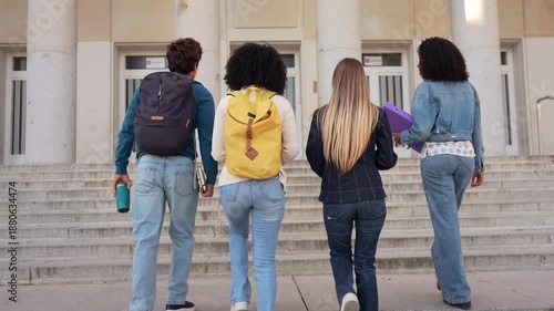 Multiracial group of young friends with backpacks walking up the stairs to the university building. Rear view of college students arriving on campus
