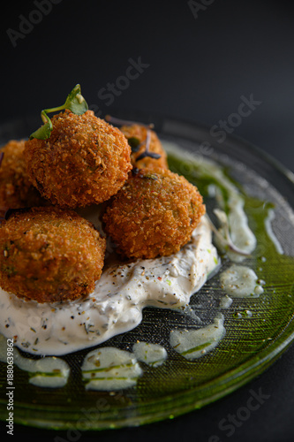 Falafel balls served on creamy yogurt sauce with fresh herbs, beautifully plated Middle Eastern vegetarian dish