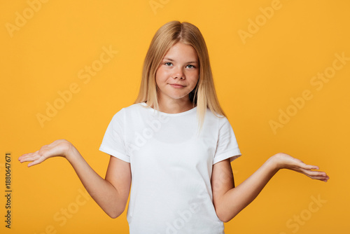Photos Serious cute teenage blonde girl spread her arms to the sides and looks at camera, isolated on yellow background, free space