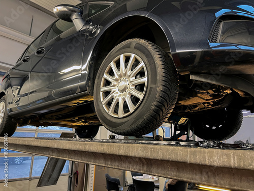 Close up low-angle view of car inspection on a service lift in a garage. The tire pattern has been changed so that it is unrecognizable.
