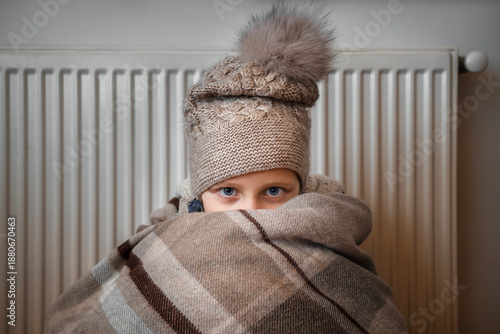 Frozed Child in Cold Home near Heater Radiator due to Blackout. Energy Crisis in Ukraine concept. 