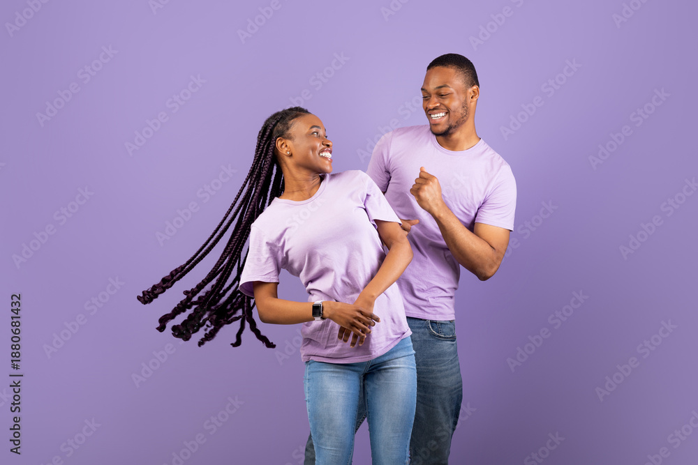 Obraz premium Enjoying Life. Portrait of happy carefree African American partners dancing and having fun, looking at each other, isolated on pastel purple violet studio background, copy space