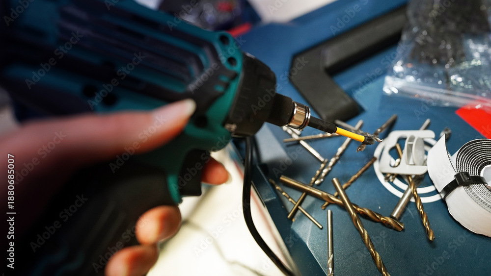 Fototapeta premium Electric Drill in Hand with Multiple Drill Bits Laid Out on Surface