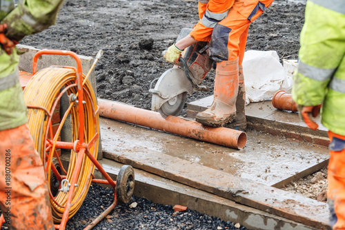 Builder cutting plastic drainage pipes at building site with power saw and diamond blade