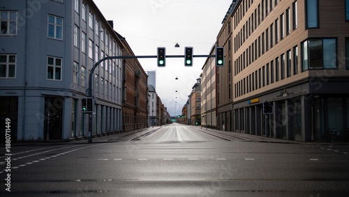 Green traffic lights on an empty street in a city during the day with no vehicles and buildings lining the road