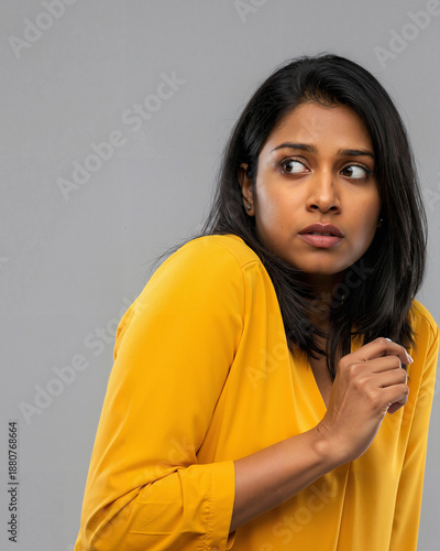 Scared Indian girl in yellow top looking over her shoulder with worried expression