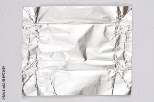 A square sheet of crumpled shiny silver aluminum foil centered on a plain gray surface