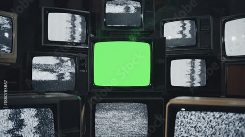 A wall of old televisions with one central screen displaying a bright green screen, surrounded by screens with static or black and white images, in a dark room with a nostalgic and retro