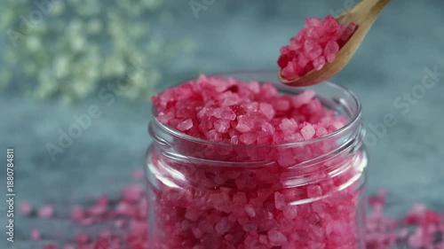 Pink salt crystals in a glass jar with a wooden spoon on a blue background with soft light