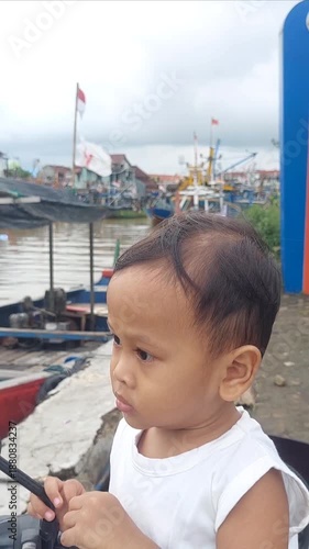 A little boy stood with an innocent and curious gaze, looking at a row of boats slowly moving along the river.