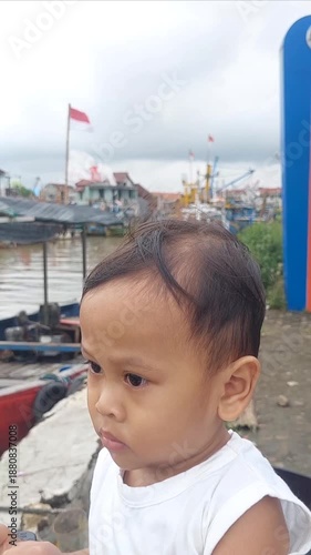 A little boy stood with an innocent and curious gaze, looking at a row of boats slowly moving along the river.
