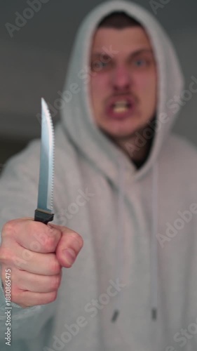 A hooded hooligan threatens someone with a knife.
The person attacks with a knife.
A sharp knife in the hands of an aggressive man.