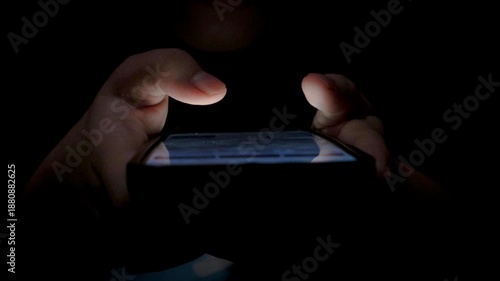 Close-up of a woman using a smartphone in a dark bedroom, browsing the internet and scrolling the screen with her finger. Close-up of a female hand scrolling on a mobile phone in a dimly lit room. 