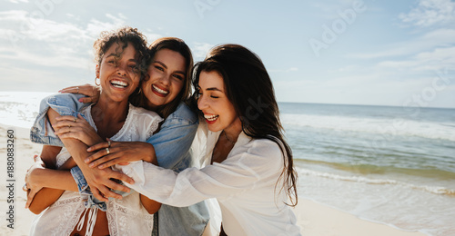 Konstfotografi Three friends laughing together on a beach enjoying a sunny day