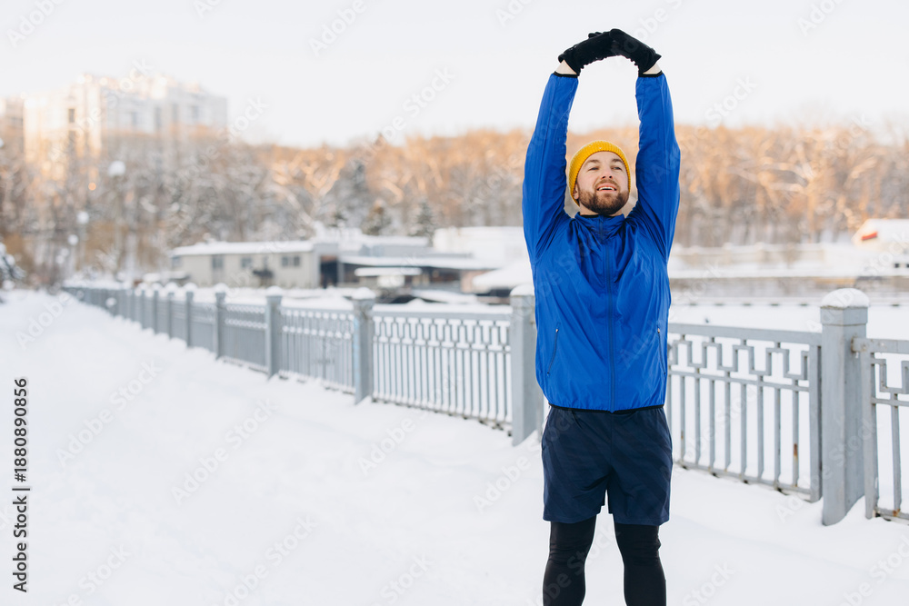 Fototapeta premium Man extending arms overhead, stretching body for exercise. Staying active and healthy during winter season