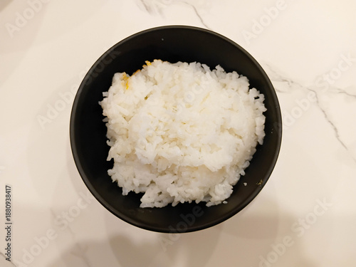 Steamed jasmine rice served in a black bowl on a clean white table, simple Asian food concept, fresh cooked rice for daily meals.