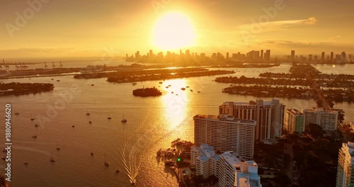 Golden hour over the stunning Biscayne Bay. Flight over the waterscape with numerous vessels on. Approaching the skyline silhouette of Miami, Florida, USA.