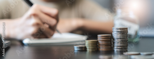 Fotografía Close up stack of coins on the table and woman do accounting as background