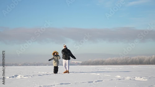 A mother and son launch a children's airplane into the sky on a sunny winter day.