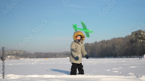 A toddler launches a toy airplane into the sky on a sunny winter day.