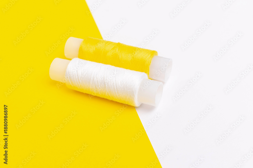 Obraz premium Spools of Yellow and White Thread on Contrasting Yellow and White Background