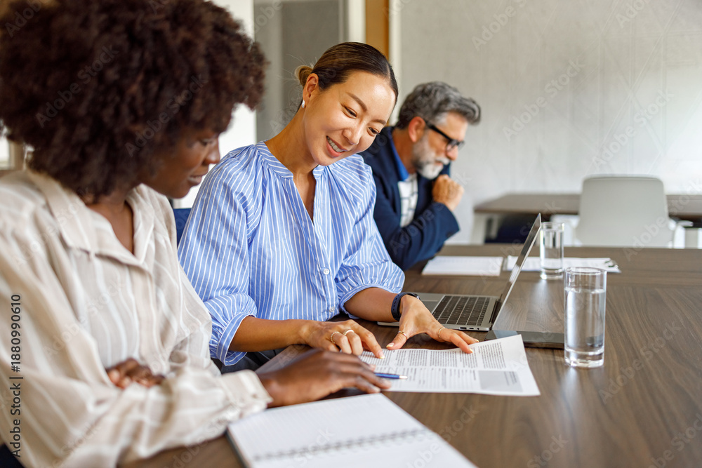 Obraz premium Female lawyers reviewing legal documents and discussing strategies while male colleague works in background in modern office