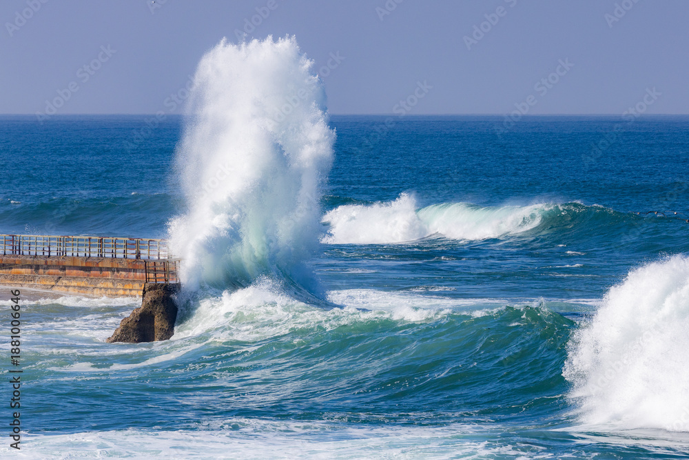 Obraz premium Big powerful king tide waves crashing and exploding onto a wall in San Diego Southern California during the day with a teal blue ocean in the background