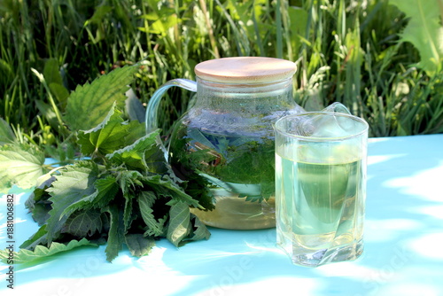 A decoction of nettle leaves in a teapot stands on a wooden table.	