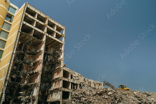Canvas-taulu Collapsed building with an excavator clearing heavy rubble at a dusty demolition site in an urban danger zone