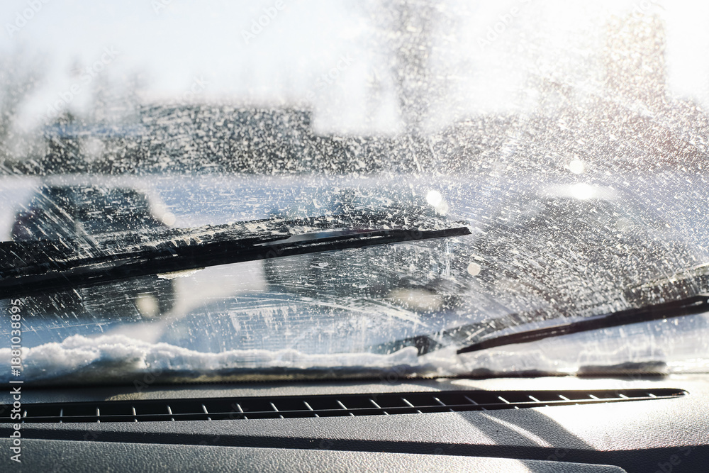 Naklejka premium Dirty car windshield in winter conditions. Washer fluid spray and road grime on glass surface. Reduced driving visibility problem. Windshield wipers in action. Cold season road safety issue.