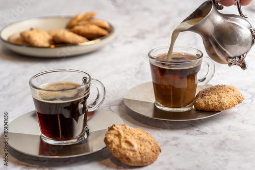 Canvas Print Pouring cream into black coffee in a glass mug.