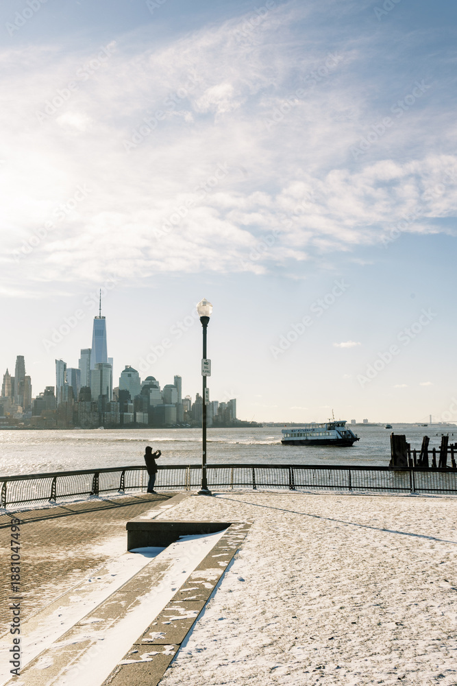 Fototapeta premium View of New York City skyline from waterfront with snow and a person taking photos on winter day