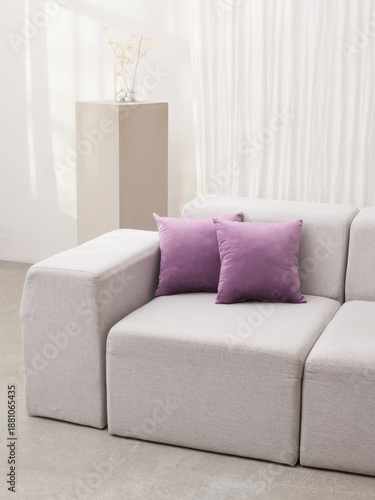 Minimalist interior soft scene featuring a modular sofa in neutral tones with two lilac throw pillows. Clean, modern design with natural light and subtle decorations. comfortable living spaces