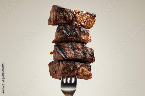 Grilled steak bites on fork, close-up, brown tones, light background