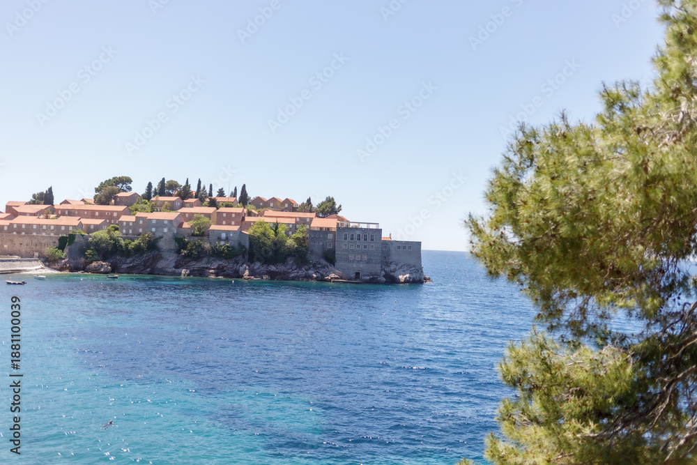 Obraz premium Panoramic view of a small island with an old coastal town, red tiled roofs and clear blue sea. Sunny summer day, Mediterranean landscape, travel and tourism concept. Island Sveti Stefan