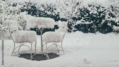 Winter garden landscape with snow accumulation on white metal chairs A bright and clean winter composition focusing on the contrast between the white snow and the garden's structures.