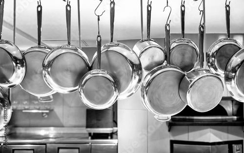 Black and white image of Copper pots and pans hanging in an industrial kitchen