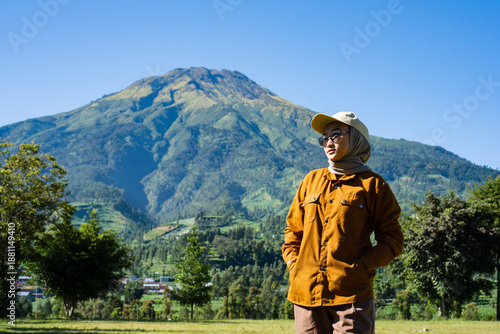 A woman stands in a field with a mountain in the background
