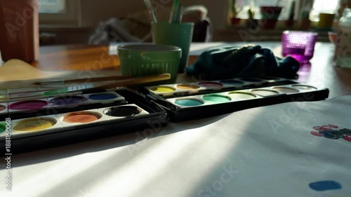 Wallpaper Mural Cozy home scene with children’s art supplies on a wooden table. Watercolor paints, brushes and drawings. Natural sunlight. Authentic family moment.  Torontodigital.ca