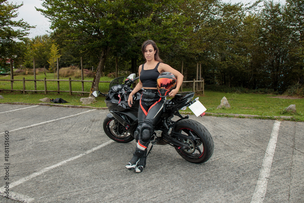 Obraz premium Young woman biker holding helmet next to sportbike