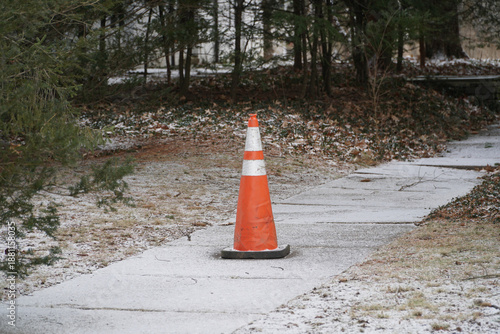 Cuadro en lienzo Orange traffic cone placed on a snow covered sidewalk or road for safety and hazard warning in hazardous winter weather conditions
